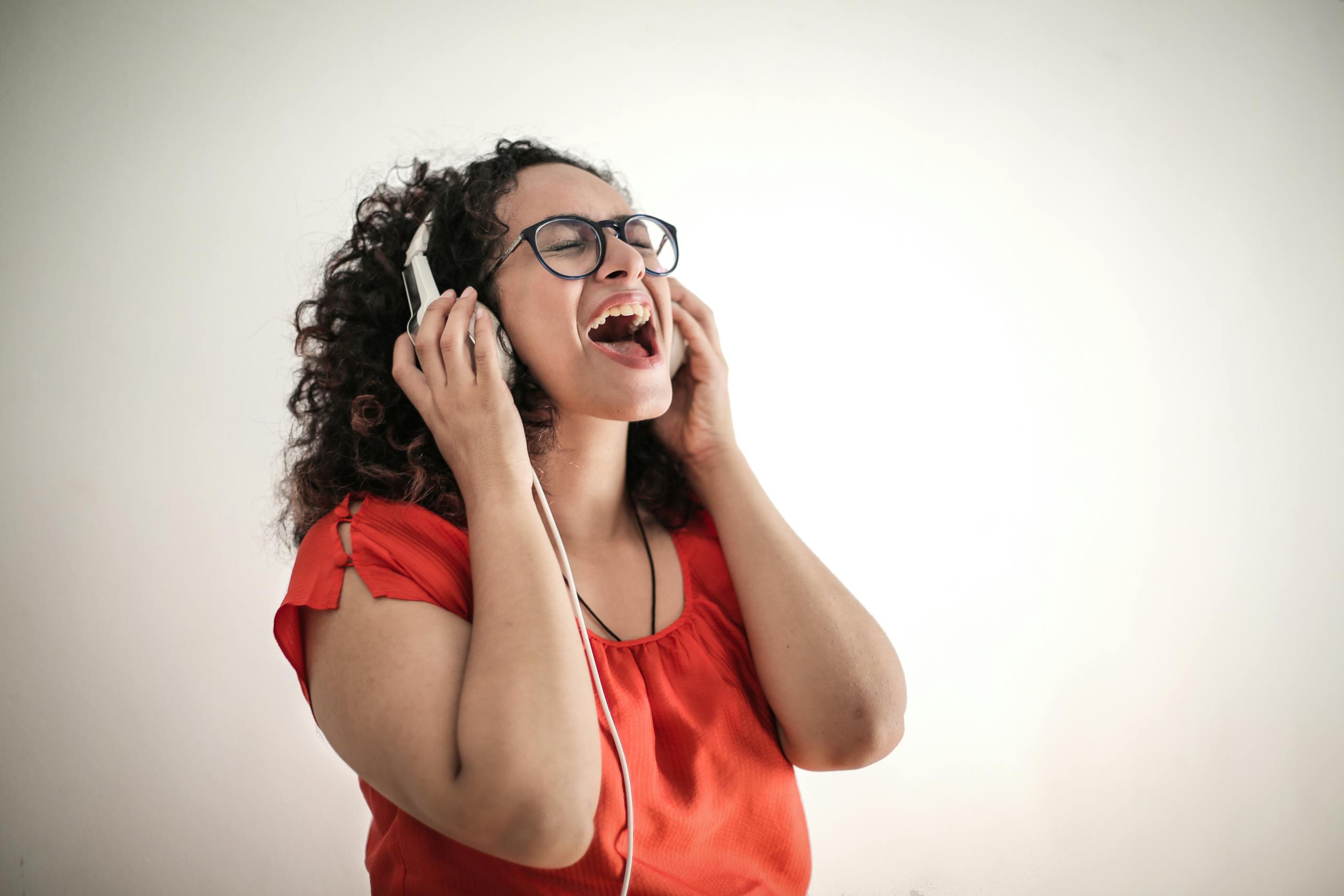 Energetic woman in a red top enjoying music with headphones, eyes closed in joy.